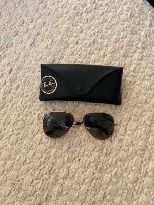 Ray-Ban solglasögon  - Snygga aviator solglasögon från Ray-Ban med tunna guldfärgade metallbågar och mörka linser. Klassisk och tidlös modell som ger en cool vibe till din stil. Medföljer svart fodral.