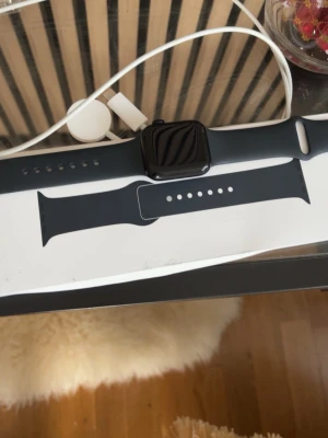 Svart Apple Watch med silikonarmband - Snygg svart Apple Watch med rektangulär skärm och svart silikonarmband. Klockan har en stilren design och kommer med extra armbandsdel samt laddare. Perfekt för dig som vill ha koll på träning, notiser och hälsa direkt på handleden. Har inte använt den många gånger och den är på jätte bra condition. Gen 2