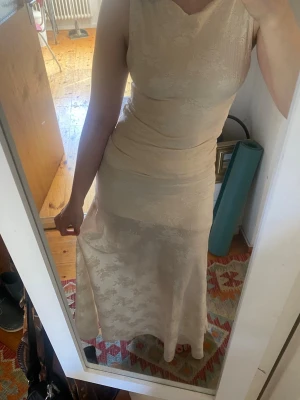 Lång kräm/vit gina studentklänning 2 piece blommor - En suuperfin studentklänning från gina. är boatneck. Köpt förra året och bar använd en gång (studenten :D), köpt för ca 900kr i butik. Lapp avklippt men överdel är S och kjol är M. För mig som är 160 är kjolen lite lång, fick vika upp den en liten bit, men om du är längre passar den nog dig bra! Baksidan av tröjan samt nedre delen av kjolen är gjort av ett tunnare material. Nästintill perfekt skick, bara använd en gång. Ända tydliga defekt jag kunde se är fotad i bild 5. Skriv vid frågor!