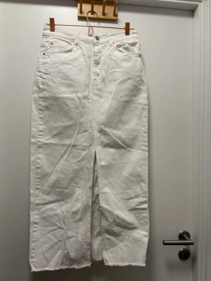 Vit denimkjol - Oanvänd. Hade hängande trådar längst ner på kjolen som har klippts av. Kjolen har en slit i mitten. Kjolen är 90cm lång