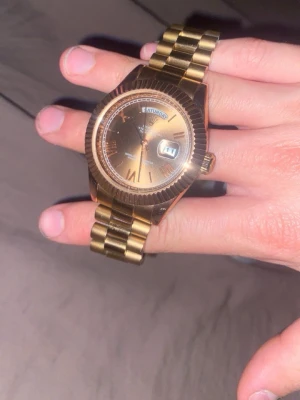 Guldfärgad klocka med länkarmband - Snygg guldfärgad klocka med klassiskt länkarmband och rund urtavla. Klockan har dag- och datumvisning samt tydliga indexmarkeringar. Perfekt accessoar BILLIGARE VID SNABB AFFÄR!