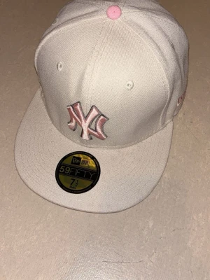 Vit New Era 59Fifty NY keps - Snygg vit New Era 59Fifty keps med rosa NY Yankees-logga framtill och rosa detaljer. Klassisk flat brim och broderad New Era-logo på sidan. 