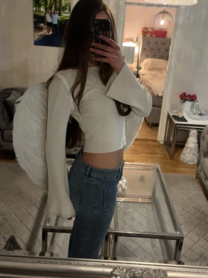 Vit ribbad croppad långärmad topp - (Känns som S) Säljer en vit croppad topp med långa, vida ärmar och ribbad struktur. Toppen har en enkel och clean look som passar perfekt till jeans eller kjol. Materialet känns mjukt och stretchigt, vilket gör den superbekväm att bära.