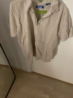 Beige halvzip tröja Jack & Jones - Snygg beige tröja från Jack & Jones med halvzip och korta ärmar. Tillverkad i mjukt stickat material som ger en avslappnad look. Perfekt till jeans eller chinos för en clean stil.