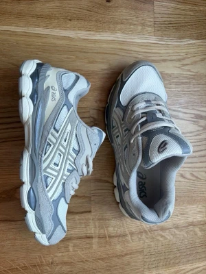 Asics gel nyc - Snygga sneakers från Asics i grått och vitt med mesh- och mockadetaljer. Skorna har en chunky sula och klassisk Asics-logga på sidan. Perfekta för dig som gillar sportig och trendig stil. Har inte kvar lådan! 