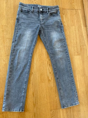 Grå tvättade raka jeans - Säljer ett par grå tvättade jeans med rak passform och klassisk femficksdesign. Jeansen har en knappgylf och subtila slitningar framtill för en avslappnad look. Perfekta till vardagsstilen och passar till det mesta i garderoben.