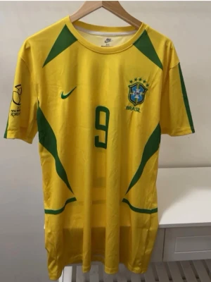 Gul Brasilien fotbollströja Nike - Säljer en gul Brasilien fotbollströja från Nike med gröna detaljer och nummer 9 på bröstet. Tröjan har officiellt landslagsmärke, tryck på ärmen från FIFA World Cup Korea och är tillverkad i ett lätt och ventilerande material. Perfekt för match eller träning.