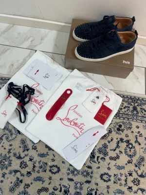 Christian Louboutin Navy - Snygga mörkblå sneakers från Christian Louboutin i mocka med coola svarta nitar på tån. Skorna har vita sulor och matchande mörkblå skosnören. Kommer med originalpåse, extra snören och skohorn. Perfekta för dig som vill sticka ut.