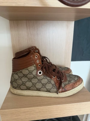 Gucci skor  - Säljer ett par snygga high top sneakers från Gucci i brunt läder och beige canvas med klassiskt GG-mönster. Ända slitaget syns på sista bilden 