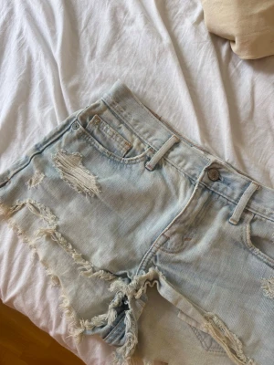 Ljusblå slitna jeansshorts Abercrombie - Säljer ett par ljusblå jeansshorts från Abercrombie & Fitch med slitna detaljer, fransiga kanter och klassiska fickor bak med broderad söm. Perfekta för sommaren och väldigt snygga. Säljer då de ej kommer till användning! Pris kan diskuteras