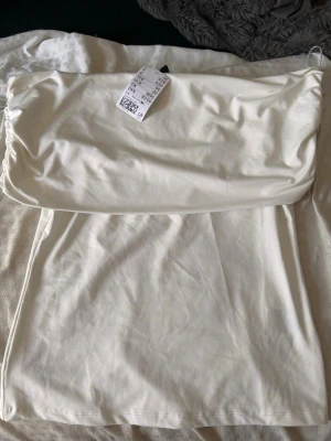 Vit offshulder topp - Säljer en enkel och stilren vit offshulder topp i mjukt material. Toppen har en rak passform som sitter snyggt på kroppen. Perfekt att matcha med jeans eller kjol för en clean look. Helt ny inte använd men säljer då ja inte kunde lämna tillbaka den. Den är i storlek M men passar även S