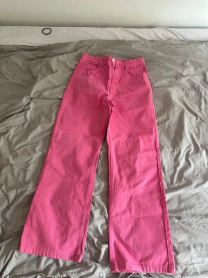 Rosa utsvängda jeans med hög midja - Säljer ett par snygga rosa jeans med hög midja och utsvängda ben. Jeansen har klassisk femficksdesign och stängs med knapp och dragkedja. Använt några enstaka gånger men en färg som trender otroligt just nu!