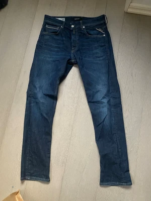Mörkblå straight fit jeans Replay - Säljer ett par mörkblå jeans från Replay, modell Grover, med straight fit. Klassisk femficksdesign, silverfärgade detaljer och kontrastsömmar. Snygga och tidlösa jeans i slitstarkt denimtyg som passar perfekt till din vardagsstil.