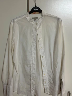Vit henley-skjorta från Burberry - Säljer en stilren vit henley-skjorta från Burberry med rund krage och knappar framtill. Skjortan är långärmad och tillverkad i mjuk bomull, perfekt för en clean och avslappnad look.