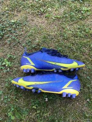 Nike Mercurial blå/gula fotbollsskor - Säljer ett par Nike Mercurial vapor 14 elite! Dessa är i 8/10 i skick i och med att dem har inga hål, hälen inuti är perfekt, och dobbarna är i perfekt skick. Dessa går ej att får tag på om dem ej är begagnade där utav är priset lite högre än vanligt! 