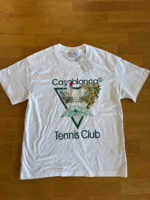 Vit Casablanca Tennis Club t-shirt - Snygg vit t-shirt från Casablanca med trycket 'Tennis Club' och ett färgglatt motiv framtill. Klassisk passform och rund hals. Perfekt för dig som gillar sportig och trendig stil.