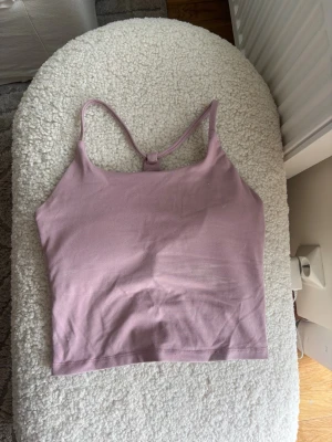 Ljuslila linnetopp från Relode - Säljer en ljuslila linnetopp från Relode med tunna axelband och racerback-design. Toppen är croppad och tillverkad i mjuk bomull, perfekt för en avslappnad och trendig look. Enkel och stilren utan mönster eller extra detaljer.