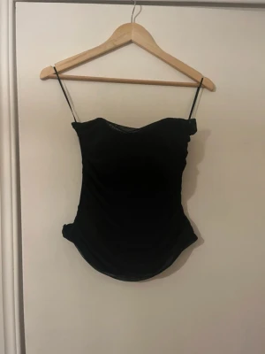 Svart korsett top - En svart korsett topp från Gina tricot. Den har ett draperat tyg framtill och har knytning där bak. Den är aldrig använd så är i bra skick!🥰