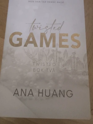 Twisted Games av Ana Huang - Twisted Games är andra boken i Twisted-serien av Ana Huang. Omslaget är vitt med guldfärgade och svarta detaljer samt ett subtilt mönster av blommor och kronor. Perfekt för dig som gillar romantisk och dramatisk skönlitteratur.
