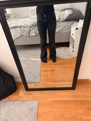 Svarta bootcut jeans med mid midja - Säljer ett par svarta bootcut jeans med mid midja och dubbla knappar i midjan. Jeansen har klassiska fem fickor och är i stretchigt denimtyg som sitter snyggt. Det står 158 i strl med eftersom att de är ifrån Gina Young men de passar som XXS eller XS (petite).