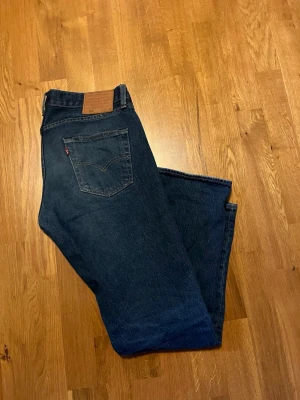 Levi's 501 mörkblå jeans - Klassiska Levi's 501 jeans i mörkblå bomull med raka ben och femficksmodell. Snygga kontrastsömmar och ikonisk röd Levi's-tagg på bakfickan. Tillverkade i bomull för en autentisk jeanskänsla. Perfekta för en avslappnad och tidlös stil. Storleken är W30 L30. Hör av dig om du har några frågor!
