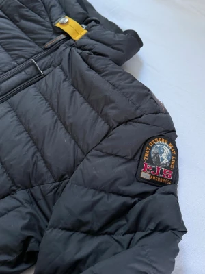 Parajumpers Lightweight Jacket - Säljer en svart pufferjacka från Parajumpers i storlek S. Jackan har quiltad design, hög krage och dragkedja framtill samt två sidofickor med dragkedja. Märkespatch på ärmen och lättviktsmaterial som håller dig varm under kalla dagar.