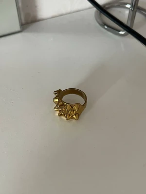Guldig statementring med nitar - Cool guldig ring från H&M med flera spetsiga nitar på ovansidan. Ringen har en chunky design och är tillverkad i metall med matt finish. Perfekt för dig som vill sticka ut och addera edge till din stil.