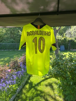 Gul FC Barcelona Ronaldinho tröja - Säljer en gul FC Barcelona matchtröja med Ronaldinho och nummer 10 på ryggen. Tröjan har klubbmärke på bröstet, svarta detaljer och Nike-logga. Perfekt för dig som älskar fotboll och vill ha en ikonisk supportertröja.