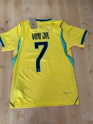 Vini Jr #7 – Player Edition Brasilien (storlek M) - Vini Jr #7-tryck. Player Edition Brasilien. Storlek M. Helt ny och aldrig använd. Säljs i befintligt skick. Skickas snabbt! 🚚💨  Mått för denna tröja (storlek M): (Uppmätta av leverantör – viss variation kan förekomma) • Halva bröstmåttet: 51 cm • Tröjans längd: 72,5 cm • Ärmbredd: 22,5 cm • Axelbredd: 43 cm • Ärmlängd: 39 cm • Manschettbredd: 18 cm  🔥 Player Edition-modell – tajtare passform än vanliga supportertröjor. 🇧🇷 Brasilien landslag.