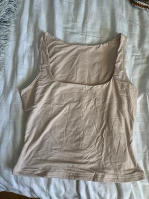 Beige ärmlös linnetopp - Snygg beige linnetopp med breda axelband och rundad halsringning. Tillverkad i mjuk bomull som känns skön mot huden. Perfekt att styla till jeans eller kjol för en enkel och clean look.