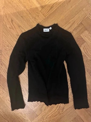 Svart stickad tröja från Kappahl - Svart stickad tröja från Kappahl med lång ärm och hög hals. Tröjan har vågig kant nertill och vid ärmslut, vilket ger en cool och trendig look. Perfekt att styla med jeans eller kjol.