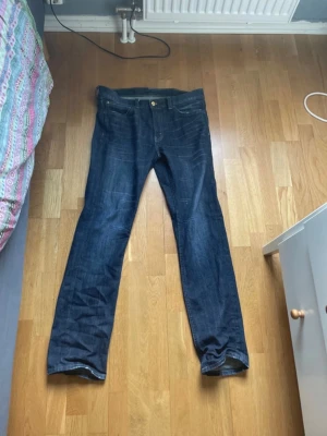 Mörkblå raka jeans från Cheap Monday  - Snygga mörkblå jeans med klassisk femficksdesign och raka ben. Jeansen har en gylf med knapp och dragkedja samt tydliga slitningar för en cool look. Perfekta till vardagsstilen och lätta att matcha med olika outfits. De är från Cheap Monday och är L32 W32