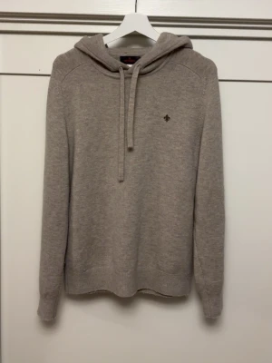 Beige hoodie från Morris - Snygg beige hoodie från Morris med dragsko i huvan och diskret logga broderad på bröstet. Tillverkad i mjukt stickat material som känns riktigt skönt mot huden. Perfekt för dig som gillar en clean och stilren look.