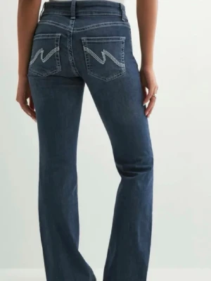 Mörkblå bootcut jeans från Wrangler - Snygga mörkblå bootcut jeans från Wrangler med klassiska kontrastsömmar och ikoniska W-detaljer på bakfickorna. Jeansen har medelhög midja, fem fickor och stängs med dragkedja och dubbla knappar. Perfekta för en avslappnad och trendig look.