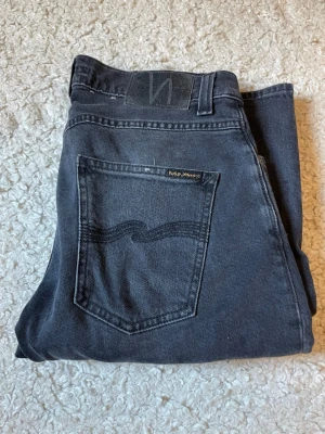 Svarta jeans från Nudie Jeans - Snygga svarta jeans från Nudie Jeans i klassisk rak modell. Jeansen har en stilren design med diskreta sömmar och är tillverkade i mjukt denimtyg. Perfekta för dig som gillar en enkel och tidlös look.