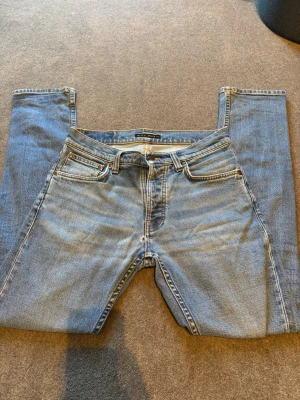 Ljusblå jeans från Nudie Jeans -  klassiska ljusblå jeans med tvätt från Nudie Jeans. Jeansen har patch i läder bak. W29 L30. (Pris kan diskuteras) ett litet hål på framsidan annars mkt bra skick 
