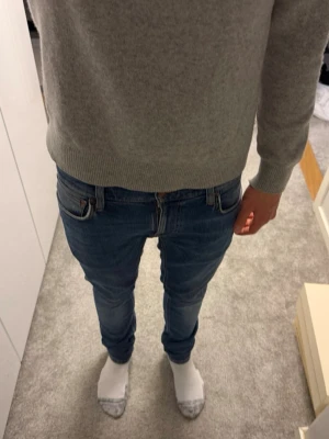 Nudie jeans  - Säljer ett par blå slim fit jeans med klassisk femficksdesign och lätt slitna detaljer på låren. Jeansen har normal midja och smal passform hela vägen ner. Perfekta för dig som gillar en modern och stilren look.