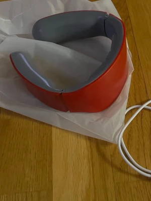 Röd massagehalsband wearable - Coolt rött massagehalsband i plast med grå insida. Perfekt för att slappna av i nacken och koppla av efter en lång dag. Laddas med medföljande vit USB-kabel. Modern design och enkel att använda.
