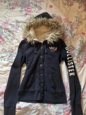 Vintage Hollister hoodie med knappar & päls - En vintage Hollister hoodie med knappar och päls i storlek M, men skulle säga passar också som en S. Färgen är en mörk marinblå, snygga detaljer och text. Defekter förekommer då den är använd och tvättad flera gånger, exempel: trådar, urtvättad osv. Skicka gärna prisförslag🌷