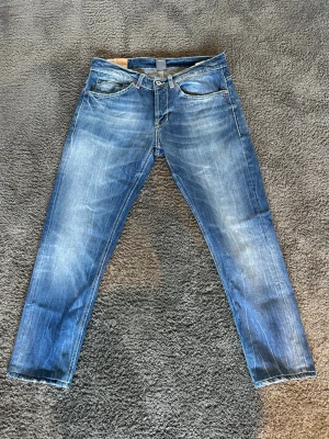 Dondup - Säljer ett par blå jeans med snyggt sliten tvätt och smal passform. Jeansen har klassiska fem fickor, dragkedjegylf och kontrastsömmar. Perfekta för dig som gillar en avslappnad men trendig stil.
