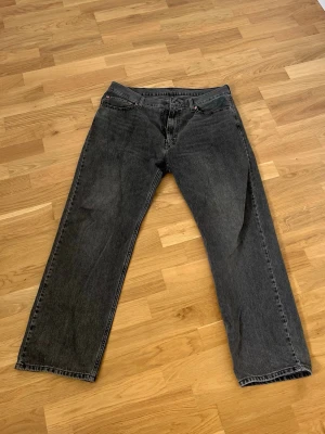 Svarta raka jeans från Levi's - Säljer ett par svarta raka jeans från Levi's med klassisk femficksdesign och knappgylf. Jeansen har en avslappnad passform och är tillverkade i kraftig denim. Perfekta för en cool och avslappnad stil.