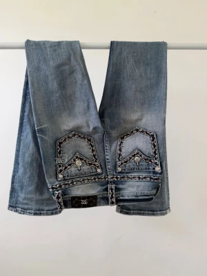 Ljusblå bootcut-jeans från miss me  - Snygga ljusblå bootcut-jeans från miss me med dekorativa bakfickor och broderade detaljer. Jeansen har låg midja och klassisk femficksdesign. Perfekta för dig som gillar en trendig och avslappnad stil.