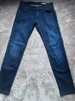 Mörkblå slim fit jeans från Replay - Snygga mörkblå jeans från Replay i slim fit-modell. Klassisk femficksdesign med diskreta slitningar och logotyp på bakfickan.