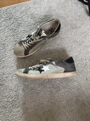 Golden Goose grå/ 2star - Säljer ett par Golden Goose liknande sneakers i grått och vitt med ikonisk stjärndetalj på sidan. Skorna har lågt skaft, vita snören och en slitstark sula. Materialet är en mix av mocka och läder. Pris 749kr!