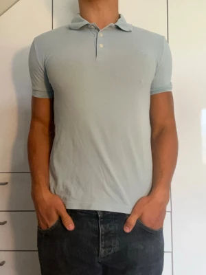 Ljusblå piké från Tiger Of Sweden - Ljusblå piké tillverkad i 100% bomull från Tiger Of Sweden. Strl S. Inga defekter. Modellen är 178 cm och väger 77 kg. Hör gärna av dig vid frågor!