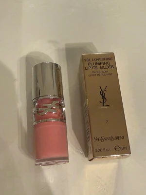 YSL Loveshine Plumping Lip Oil Gloss - YSL Loveshine Plumping Lip Oil Gloss i färgen 2 är ett lyxigt läppglans med oljebaserad formula som ger glans och volym. Kommer i en elegant förpackning med silverlock och YSL-logga. Färgen är en mjuk rosa nyans och innehållet är 6 ml.