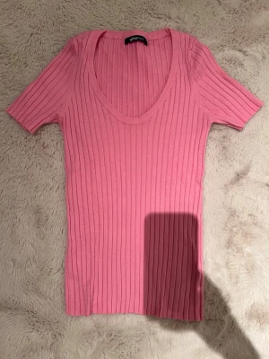 Rosa ribbad topp från Gina Tricot - Supersnygg rosa ribbad topp från Gina Tricot med djup rundringning och korta ärmar. Toppen har en slim passform och är tillverkad i ett mjukt, stretchigt material som sitter skönt på kroppen. Perfekt att styla med jeans eller kjol.