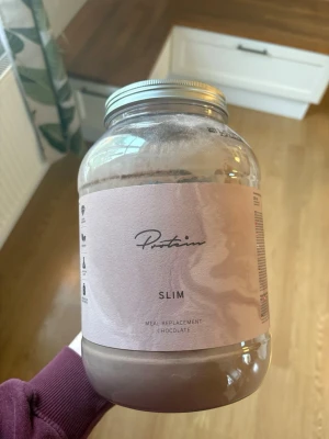 Protein Slim choklad måltidsersättning - Stor burk (1,2kg) med Protein Slim måltidsersättning i chokladsmak. Använt 3 portioner så 1kg är kvar i behållaren, säljer då den inte kommer till användning för mig! Perfekt för dig som vill ha ett enkelt och gott alternativ till måltid eller mellanmå
