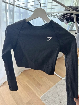 Svart crop top från Gymshark - Snygg svart långärmad crop top från Gymshark med diskret logga på bröstet. Köpt för några år sedan men använd ca 2ggr.