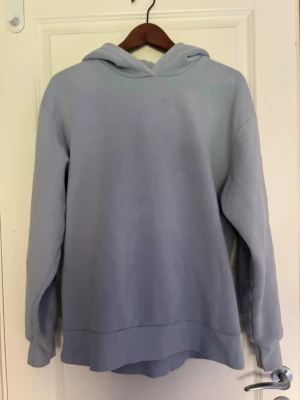 Ljusblå hoodie med huva - En enkel och stilren ljusblå hoodie med huva. Hoodien har en avslappnad passform, långa ärmar och ribbade muddar vid ärmslut och nederkant. Perfekt för en chill och bekväm look. Materialet känns mjukt och skönt mot huden.